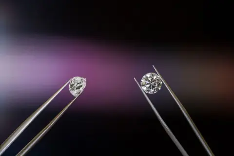 Dwa kamienie szlachetne w pęsecie: surowy brylant i oszlifowany diament.