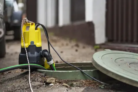 Bomba de agua funciona pero no sube agua. La bomba amarilla y negra está sumergida en una alcantarilla abierta, con una manguera verde conectada.
