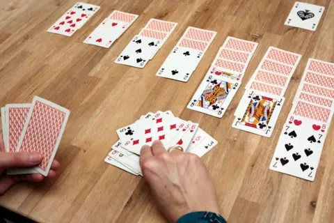 Gracze rozgrywają pasjansa, układając karty w rzędy. Widać króla i damę, a także kilka mniejszych kart. To idealne gry w karty na 2 osoby, gdzie 24 karty tworzą strategiczną rozgrywkę.