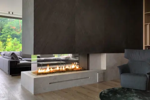 Nowoczesny salon z panoramicznym oknem i wkładem elektrycznym do kominka, tworzącym przytulną atmosferę.