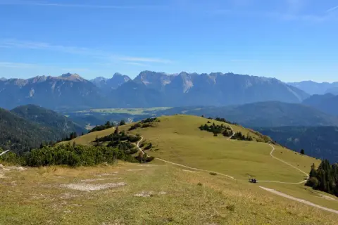 Ein sonniger Tag lädt zum **Wank wandern** ein. Grüne Hügel mit verschlungenen Pfaden erstrecken sich vor einer majestätischen Bergkulisse.