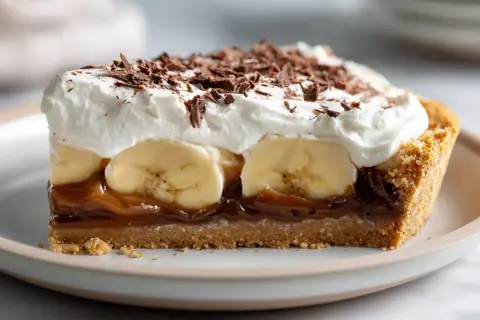 En bit krämig banoffee paj med lager av banan, kolasås och vispad grädde, toppad med chokladspån.