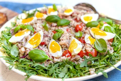 En härlig tonfisk sallad med kokta ägg, tomater, bönor och färsk basilika, serverad på en bädd av rucola.