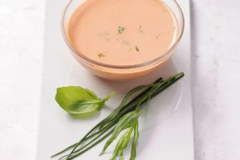 Schüssel mit cremigem French Dressing, garniert mit frischem Basilikum und Schnittlauch.