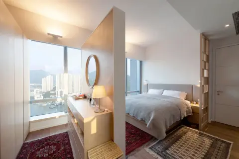 Ein moderner Schlafbereich mit einem Bett, getrennt durch einen eleganten raumteiler vorm bett, der auch als Schminktisch dient.