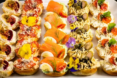 Kolorowe przekąski na talerzu: łosoś, salami, pasztet, warzywa i jadalne kwiaty. Idealne na szybkie śniadanie.
