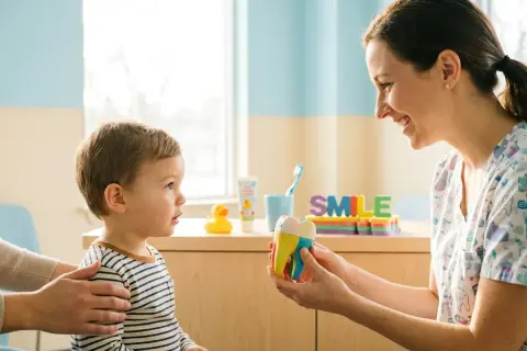 Dentista mostra un modello di dente a un bambino, spiegando l'importanza dell'ortodonzia intercettiva per un sorriso sano fin da piccoli.