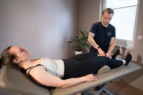 Mann führt Lymphdrainage Massage am Bein einer liegenden Frau durch.