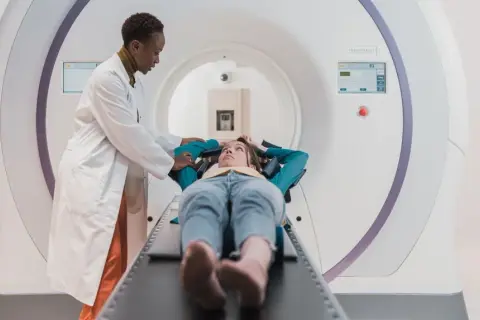 Lekarka przygotowuje pacjentkę do badania rezonansem. Częstotliwość badań zależy od wskazań medycznych.