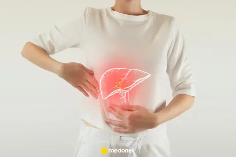 Kobieta trzyma się za brzuch, gdzie widoczny jest zarys wątroby z czerwonym podświetleniem. To może sugerować, że odczuwa objawy przeciążonej wątroby.