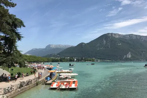 Vue animée de la plage de l'Impérial avec des pédalos et des montagnes en arrière-plan.