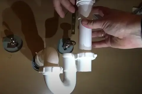 Hands assemble a white P-trap for a kitchen sink installation.