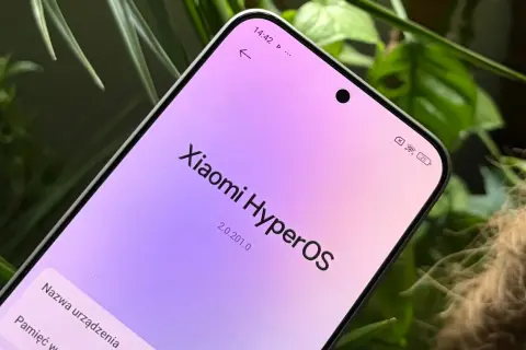 Ekran telefonu z napisem "Xiaomi HyperOS" w pastelowych barwach, otoczony zielenią roślin.