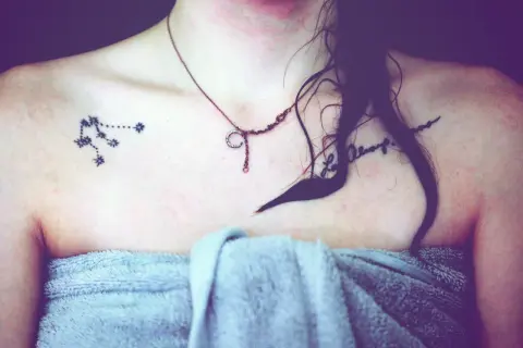 Tattoo eines Sternbilds auf der Schulter einer Frau mit einer Kette und einem Handtuch.