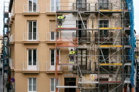 Trabajadores en andamios rehabilitan fachadas de edificios en una calle urbana.