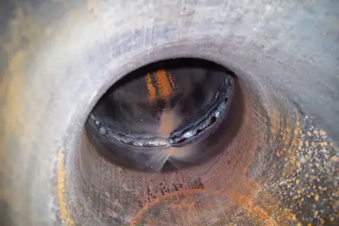 Widok wnętrza rury z widocznym, nierównym, zimnym spawem. Rdza i naloty na metalowej powierzchni.