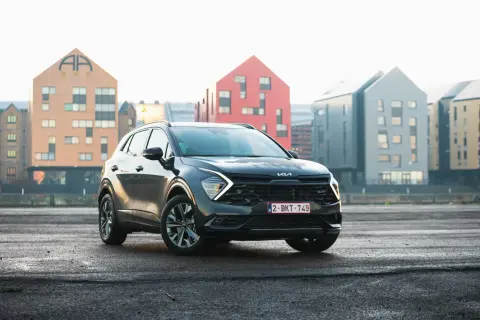 Czarny, mały SUV Kia Sportage stoi na mokrym asfalcie przed nowoczesnymi budynkami.