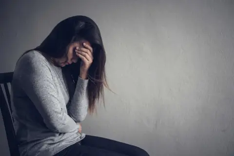 Kobieta z ręką na twarzy, pogrążona w smutku. Jak pomóc osobie z depresją która nie chce pomocy? Cierpliwość i wsparcie są kluczowe.