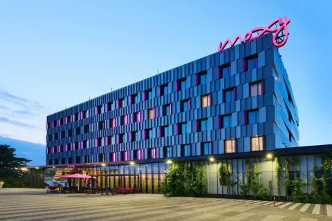 Nowoczesny hotel Moxy Hotels Pyrzowice z neonowym logo na dachu i kolorowymi podświetleniami okien.