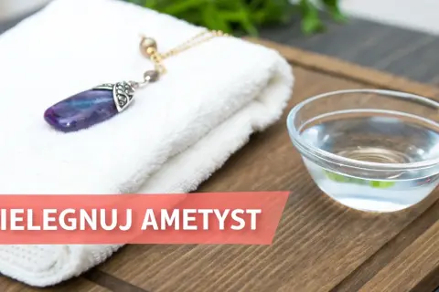 Delikatny naszyjnik z ametystem leży na białym ręczniku obok miseczki z wodą. Czas zadbać o piękno kamienia.
