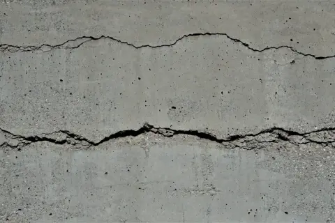 Zwei tiefe, unregelmäßige Risse durchziehen die graue Betonwand und zeugen von den Spuren der Zeit.