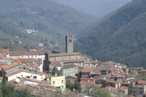 Panoramica di una villa con una basilica imponente, incastonata tra dolci colline boscose.