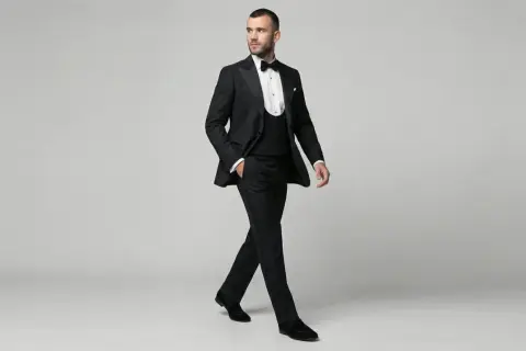 Ein Mann in eleganter Smoking-Kleidung mit Weste und Fliege schreitet selbstbewusst.