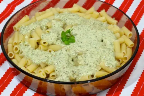 Macarrones al pesto servidos en un bol de cristal, con una hoja de albahaca fresca decorando la cremosa salsa verde.