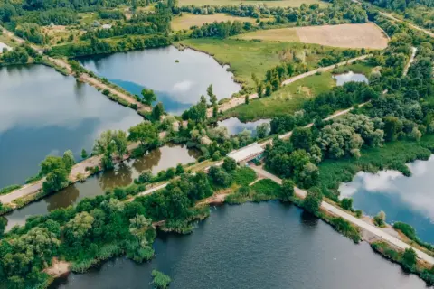 Malowniczy krajobraz z licznymi stawami i dołami, otoczony zielenią. W oddali widać pola i lasy.