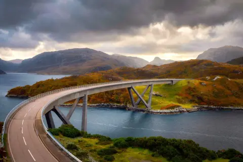 Un puente moderno cruza un fiordo escocés, con colinas otoñales y cielos dramáticos. La ruta 500 escocia ofrece vistas espectaculares.