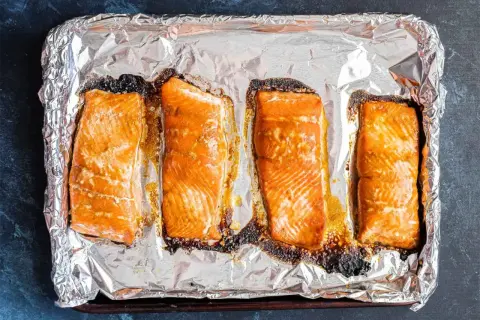 Cztery kawałki łososia na blasze wyłożonej folią aluminiową, gotowe do przygotowania sushi.