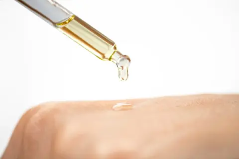 Tropfen eines goldenen Öls fallen aus einer Pipette auf die Haut. Glycerin ist ein Feuchtigkeitsspender, der die Haut geschmeidig macht.