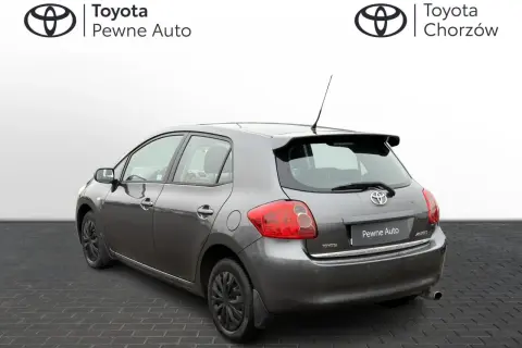 Szary Toyota Auris 2006 z przyciemnianymi szybami i spojlerem, zaparkowany na kostce brukowej.