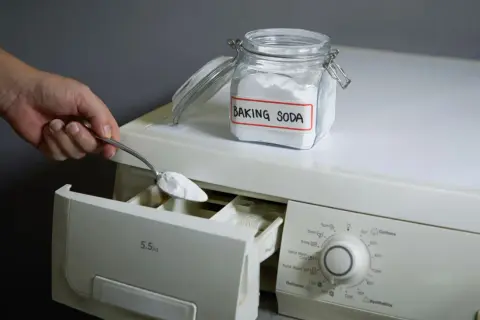 Mano aggiunge bicarbonato di sodio, un ingrediente naturale per la soda per lavatrice, nel cassetto del detersivo.