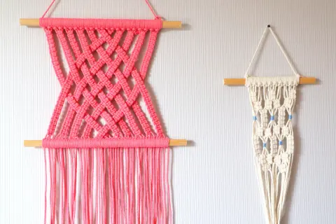 Deux tentures murales en macramé : une rose vif avec un motif croisé, et une écru avec des perles bleues. Idéal pour un tuto macramé mural.