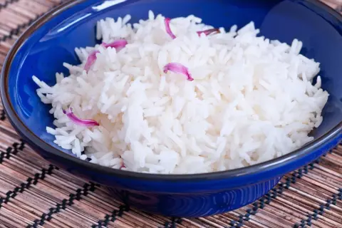 Aksamitny ryż basmati ig w niebieskiej miseczce, ozdobiony delikatnymi płatkami kwiatów.