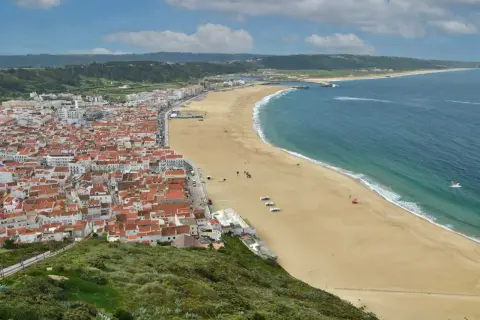 Vista aérea de Nazaré, Portugal, con su extensa playa dorada y el mar azul. Planifica tu viaje a Nazaré, Portugal, como llegar es fácil.