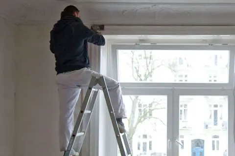 Mann auf Leiter renoviert Wohnung. Mieterrechte bei Sanierung beachten.
