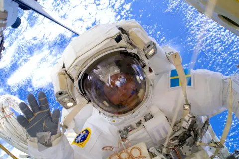 Astronaut med svensk flagga på dräkten, vinkar från rymden. Här arbetade Fuglesang på.
