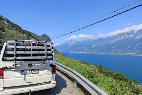 Biały bus z bagażnikiem rowerowym na tle jeziora i gór we Włoszech. Zastanawiasz się, ile trwa podróż do Włoch autokarem?