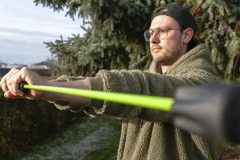 Mann mit Brille und Kappe trainiert mit einem leuchtend grünen Schwingstab, bereit für den Decathlon.