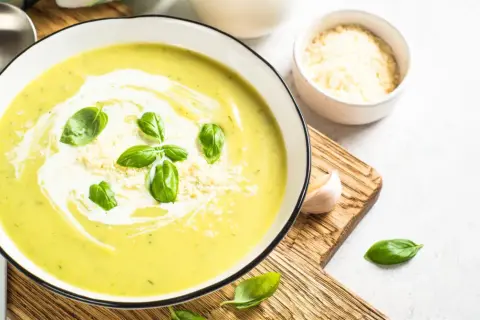 Aksamitna zupa krem z cukinii z warzywami, udekorowana listkami bazylii i parmezanem. Idealna na lekki obiad.