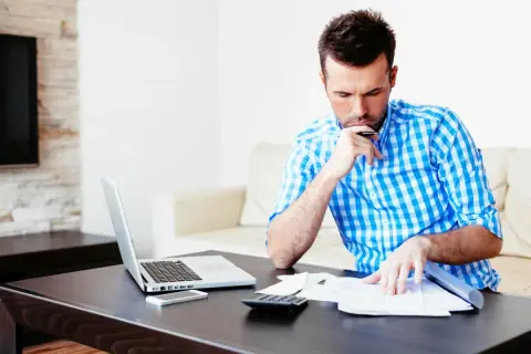 Mężczyzna w kratę analizuje dokumenty, obok laptop, telefon i kalkulator. Może to być jego ufg historia oc.