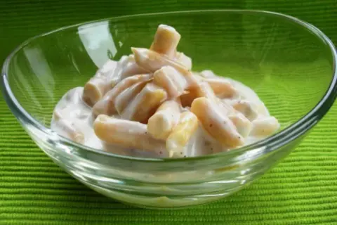 Gelber Bohnensalat in einer Glasschüssel auf grünem Hintergrund.
