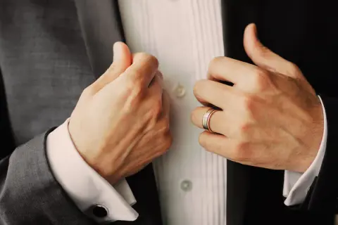 Manos ajustando su traje, mostrando un anillo de bodas. Un detalle elegante para saber donde poner anillos hombre.