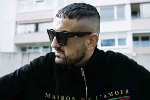 Ein Mann mit kurzgeschorenem Haar und Sonnenbrille, der die Rap-Szene repräsentiert.