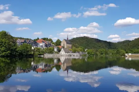 Idyllische Häuserzeile mit Kirche am Ufer des Beyenburger Stausees. Perfekt für eine entspannte Rundweg-Tour.