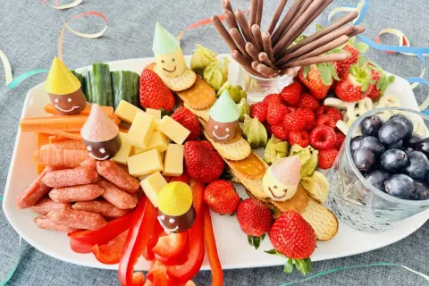 Bunter Snack-Teller mit Früchten, Käse, Würstchen und lustigen Figuren mit Partyhüten – perfekt für Fasching im Kindergarten!