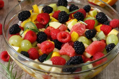 Un bol débordant de salade de fruits colorée : framboises, mûres, raisins verts, morceaux de pomme, pamplemousse et kiwi.