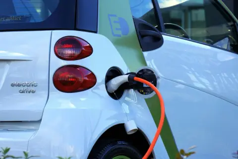 Voiture électrique blanche en charge, avec un câble orange branché. Le symbole "E" vert sur le flanc indique son caractère écologique. Le frais réel d'une voiture électrique est sa recharge.